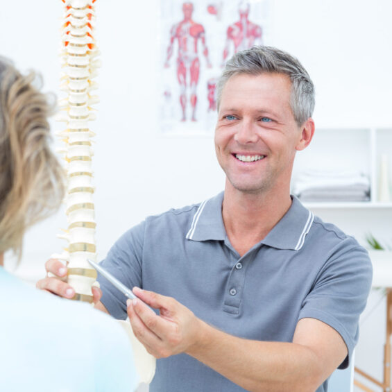 Smiling,Physiotherapist,Showing,Spine,Model,To,His,Patient,In,Medical